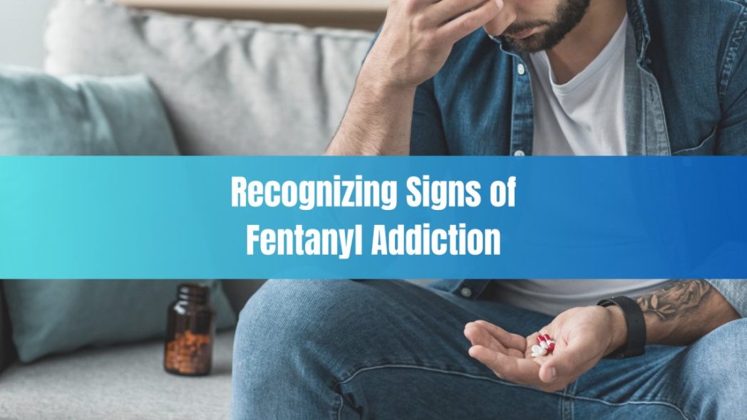Man sitting on couch holding pills with a distressed expression, representing the emotional and physical signs of fentanyl addiction in the context of recognizing early symptoms.