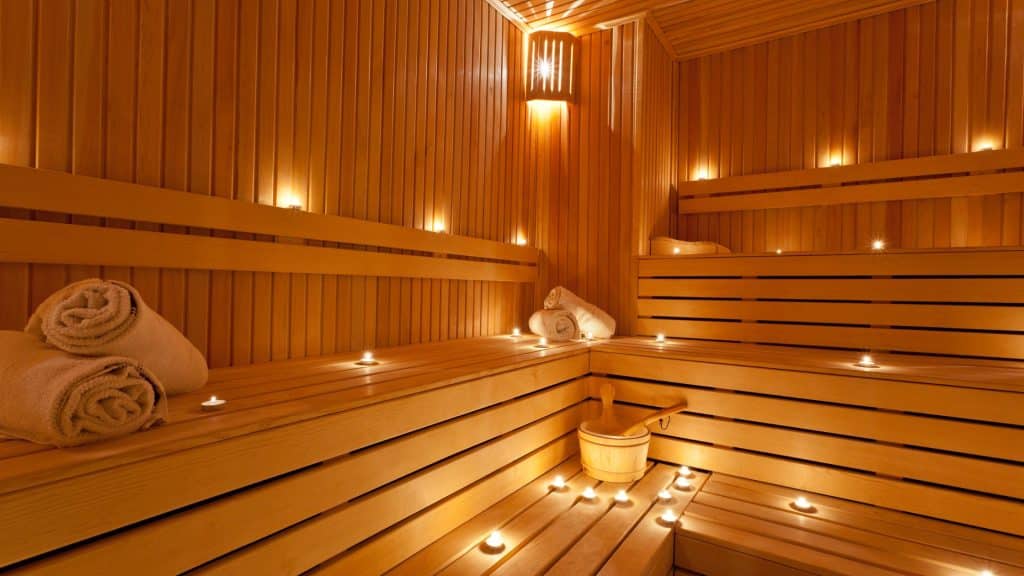 Cozy sauna interior with wooden benches, rolled towels, and lit candles, illustrating relaxation and discussions about alcohol and sauna effects – Nirvana Recovery.