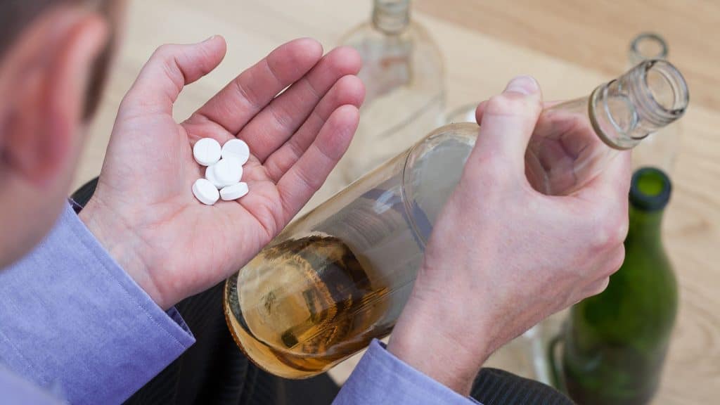 Person holding white pills and a bottle of alcohol, illustrating the risks of mixing Lexapro and alcohol – Nirvana Recovery.