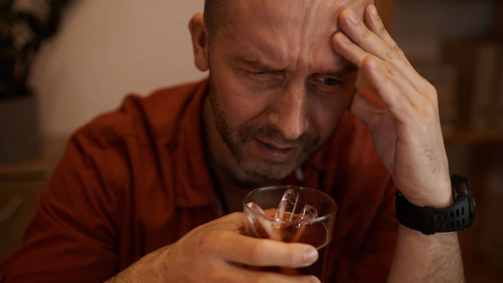 Man holding a drink with a distressed expression, illustrating the effects of mixing alcohol and Lexapro – Nirvana Recovery.