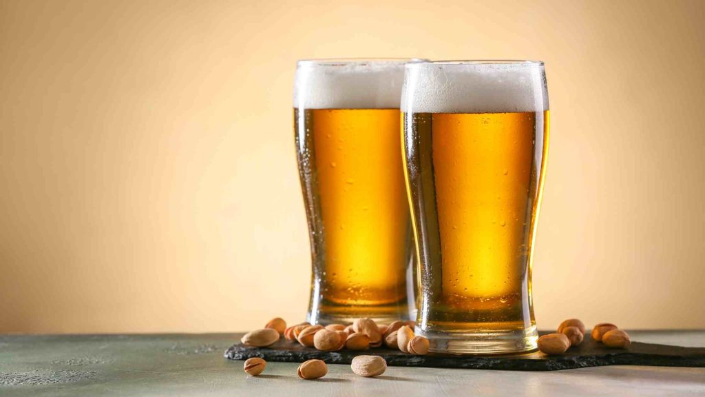 Two tall glasses of beer with foam and scattered nuts, illustrating typical alcohol percentage found in different beer types.