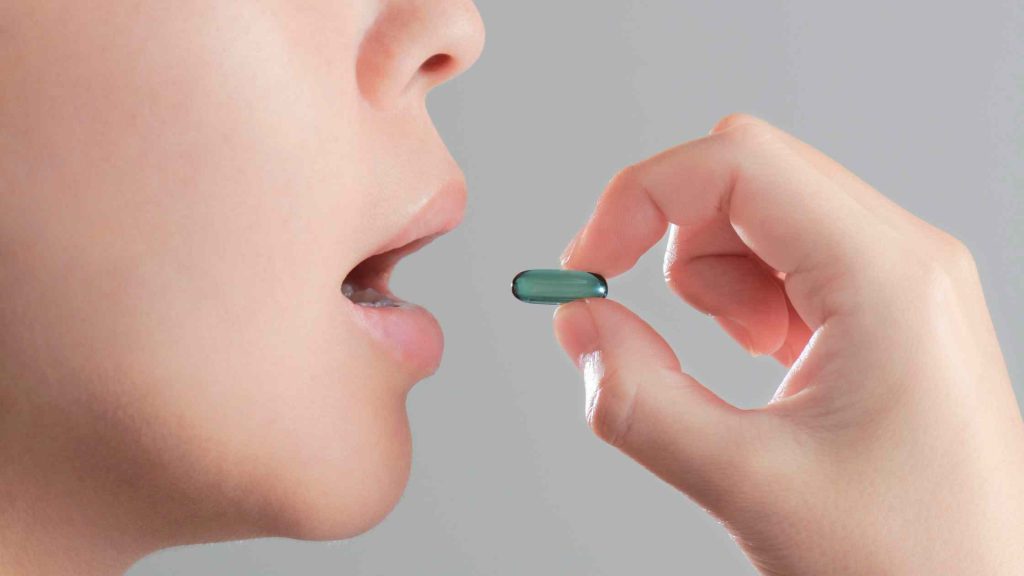 Person about to swallow a green capsule pill, representing potential risk of gabapentin misuse.