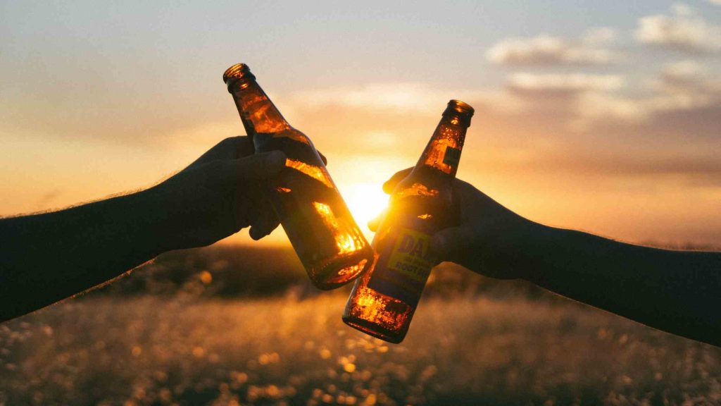 Two people clinking beer bottles at sunset, representing low-carb beers as keto-friendly alcoholic drink options.