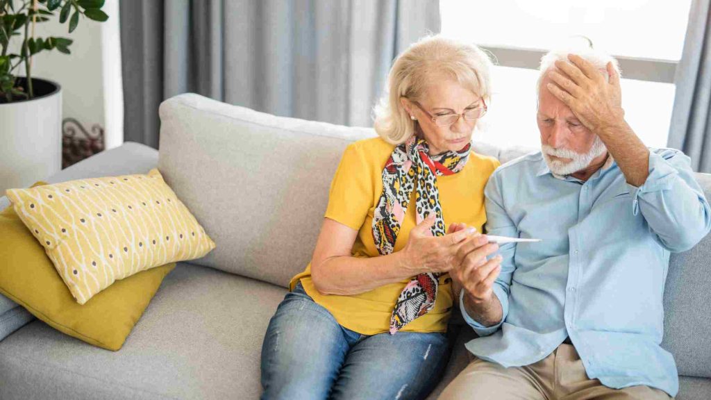 Elderly couple checking thermometer while man holds his head, highlighting fever and chills possibly linked to alcohol use.