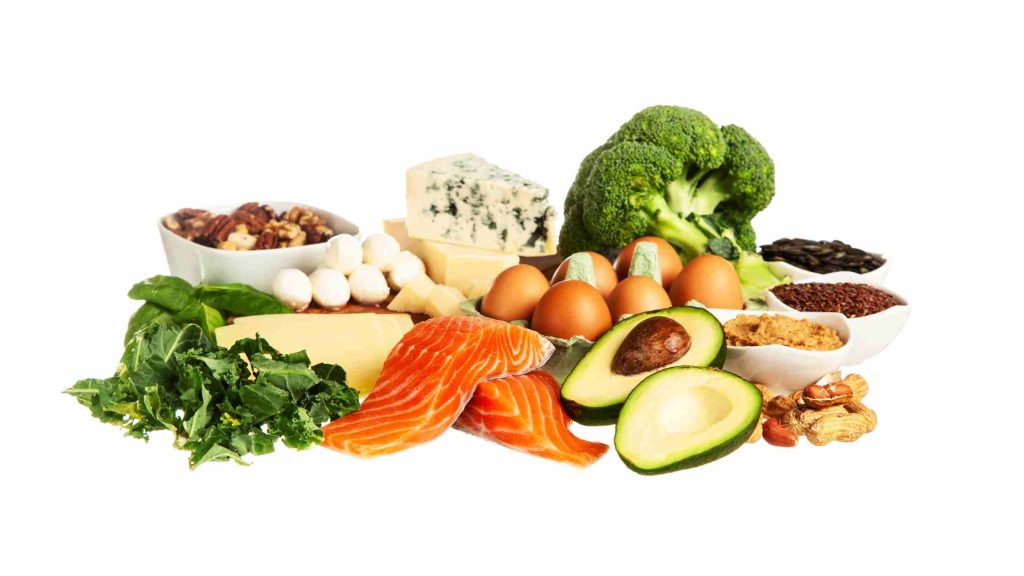 Assorted keto-friendly foods including salmon, eggs, avocado, cheese, nuts, and greens, illustrating a low-carb ketogenic diet.
