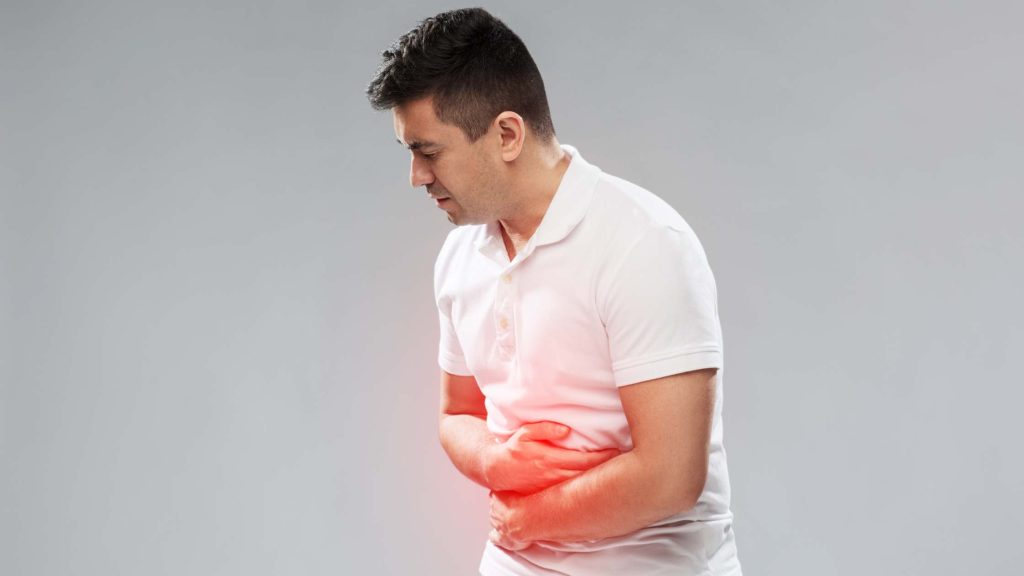 Man clutching his stomach in pain, symbolizing abdominal issues and common causes of vomiting blood after drinking alcohol.