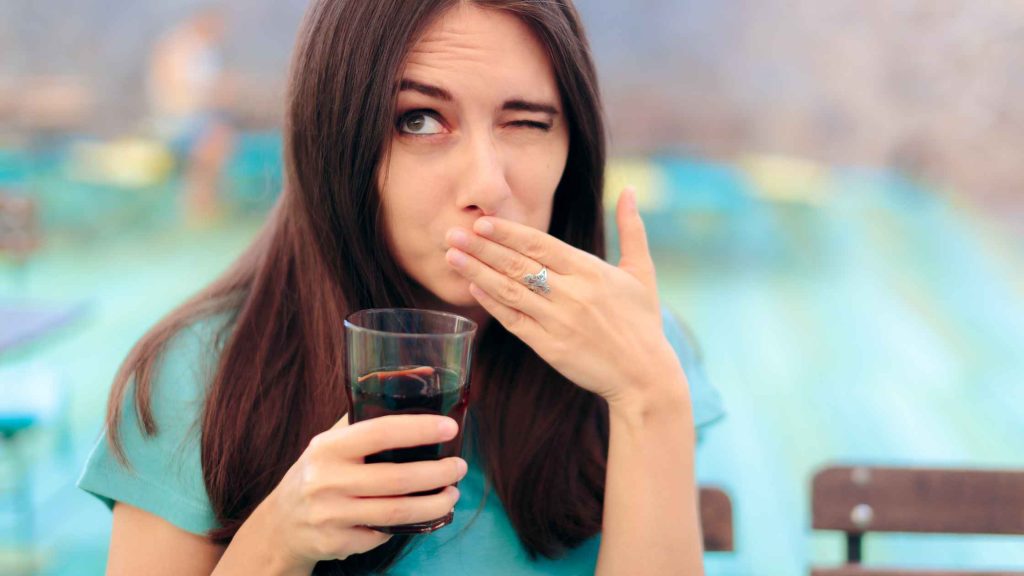 Woman holding a drink and covering her mouth due to hiccups, a common symptom of alcoholic gastritis.