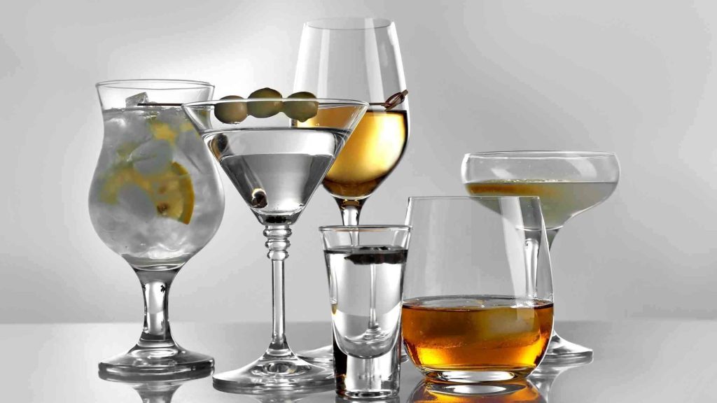 Various cocktail and liquor glasses on a reflective surface, showing alcohol strength compared to beer's lower percentage.