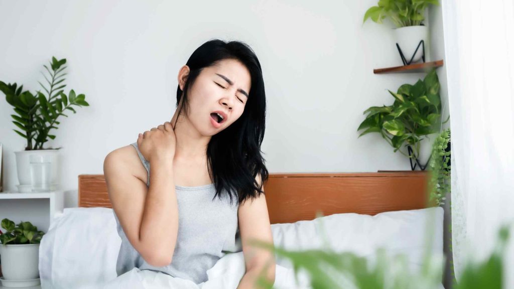 Woman sitting on bed having bed sore, showing health struggles linked to complications of delirium tremens.