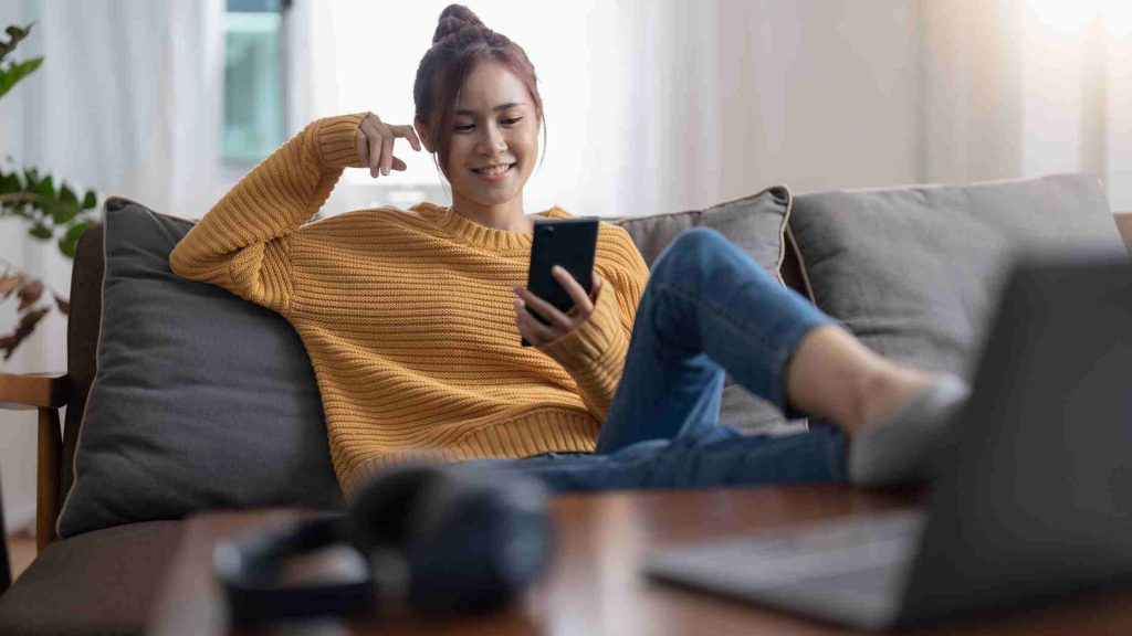 Teen girl smiling at phone while lounging on couch, representing identifying and managing problematic social media use.