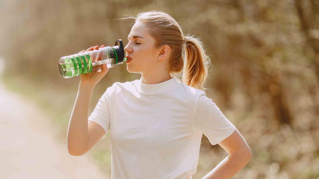 Woman drinks water outdoors, highlighting hydration as a key practical tip for safely drinking alcohol on a keto diet.