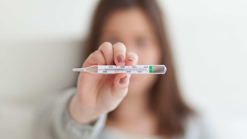 Person holding a thermometer showing a fever, symbolizing physical symptoms linked to delirium tremens.