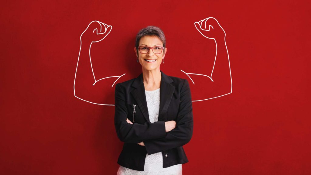 Smiling older woman standing confidently with drawn strong arms, symbolizing age as a risk factor for delirium tremens (DTs).