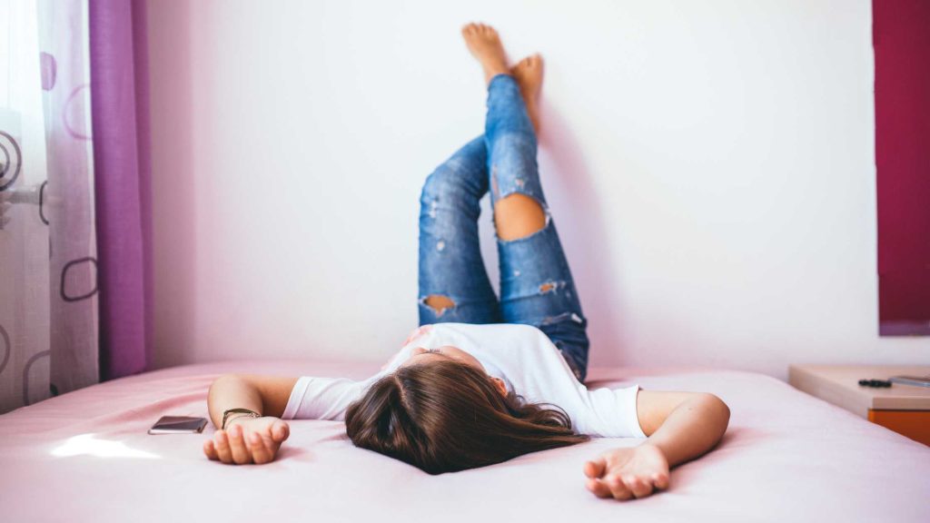 Teen girl lies on bed with phone nearby, showing how social media overuse affects sleep quality and productivity.