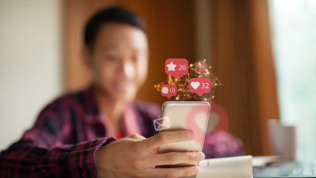 Teen smiling at phone with likes and notifications popping up, showing the psychology behind social media use.