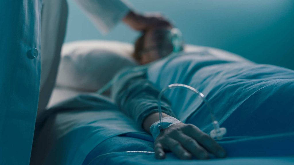 Patient lying in a hospital bed with IV and oxygen mask, symbolizing hospitalization for delirium tremens treatment.