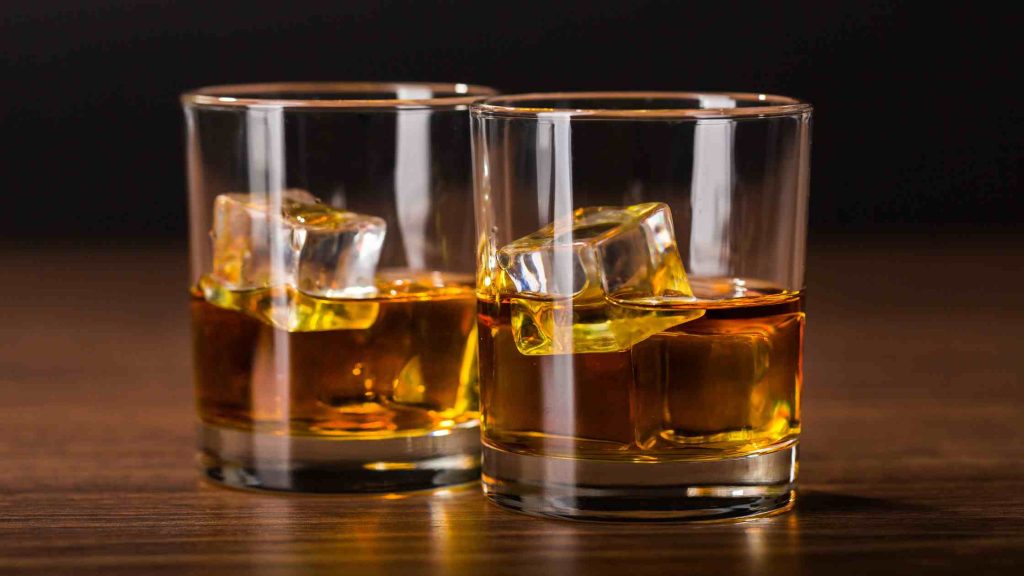 Two whiskey glasses with ice on a wooden table, representing the concept of Alcohol by Volume (ABV) in strong drinks.