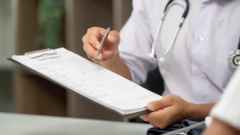 Doctor reviewing summary of benefits, illustrating steps to verify Blue Cross coverage for detox or alcohol rehab services.