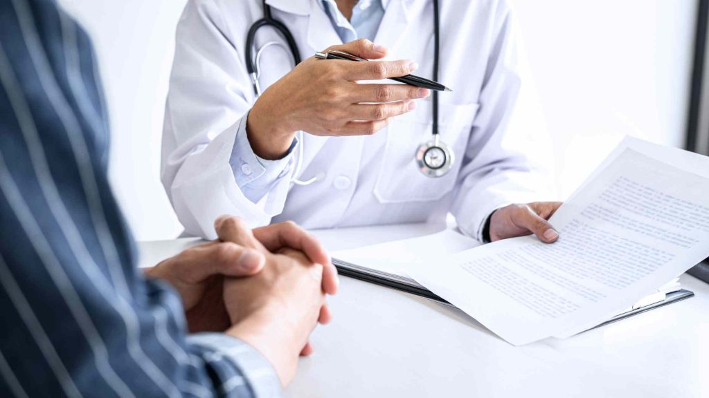 Doctor reviewing documents with patient, illustrating employer health plans to know Blue Cross outpatient treatment coverage.
