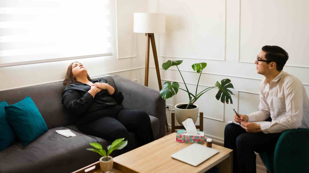 Woman in therapy session holding her chest while counselor listens, symbolizing Aetna-covered outpatient aftercare support.
