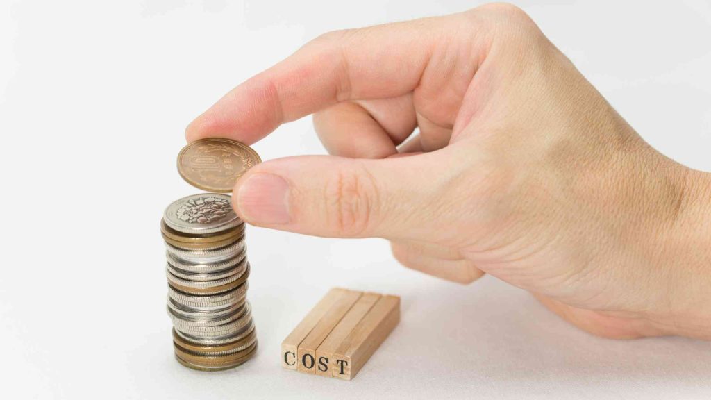 Hand stacking coins beside wooden blocks spelling “COST,” symbolizing rehab expenses with Aetna PPO coverage in Arizona.