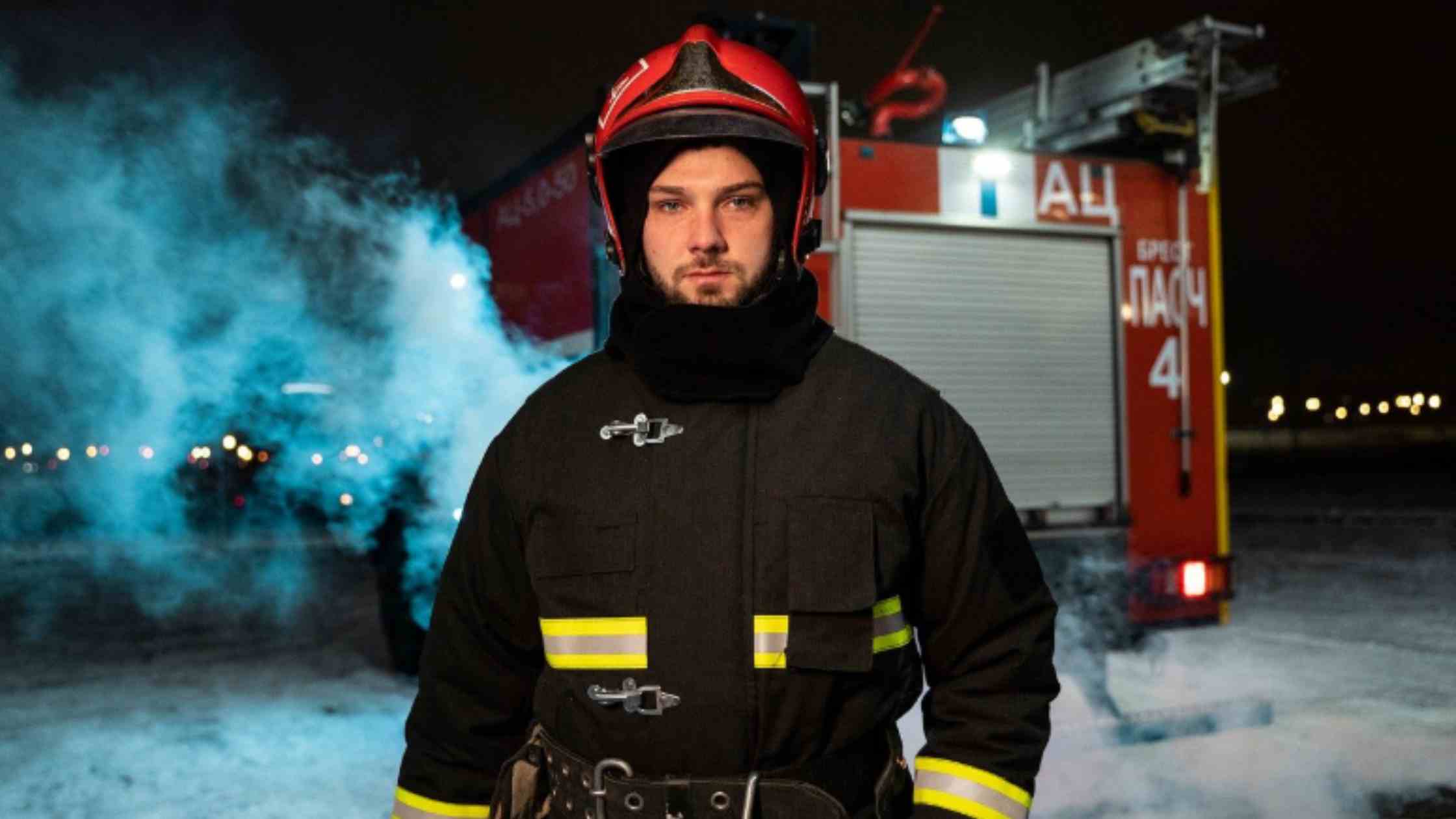 A firefighter stands confidently near a fire truck at night, smoke swirling around, symbolizing strength and recovery.