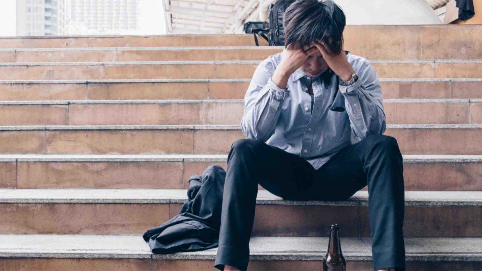 Unemployed man sitting on steps struggling with addiction, showing how job loss and substance use intersect for Arizona.
